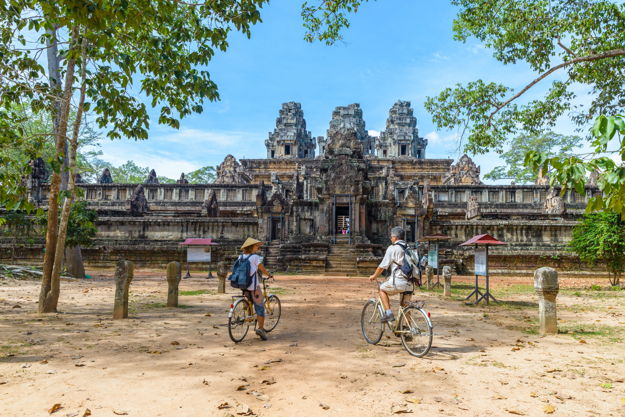 Tourist couple cycling around Angkor temple, Cambodia. Ta Keo building ruins in the jungle. Eco friendly tourism traveling.